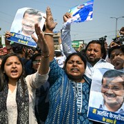 Des hommes et des femmes manifestent dans une rue en brandissant des photos d'Arvind Kejriwal.