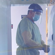 Une employés de la santé porte sa jaquette de protection, une visière et un masque.