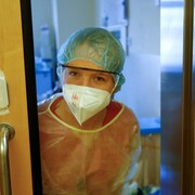 Une infirmière regarde par une vitre d'une unité de soins.