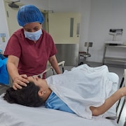 Une infirmière met la main sur le front d’une patiente couchée sur une civière.