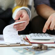 Deux personnes font des calculs avec des factures et une calculatrice.