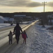 Une femme et deux enfants marchent le long d'une route dans un village en hiver.