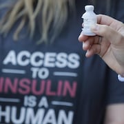 Un patient tient une fiole d'insuline devant une femme qui porte un t-shirt avec le slogan : L'accessibilité à l'insuline est un droit humain.28 juillet 2019, à Windsor, en Ontario.