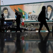 Des gens dans la pénombre passent devant une murale à Téhéran.