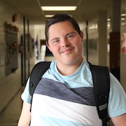 Un adolescent souriant porte un sac à dos dans un couloir d'école au mois d'octobre au Manitoba. 