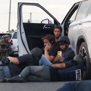 Des hommes en gilet pare-balles sont accroupis derrière une voiture. 