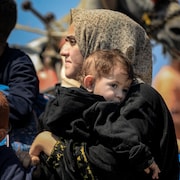 Une femme et son enfant dans les bras au milieu d'une foule.