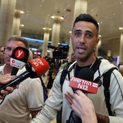 Un homme s'adresse à des représentants de la presse dans un aéroport.