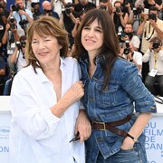 Deux femmes sourient et se font prendre en photo. En arrière-plan, plusieurs photographes ont des appareils photos dans les mains. 