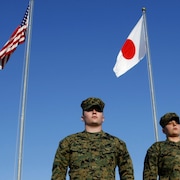 Deux militaires se tiennent devant les drapeaux du Japon et des États-Unis.