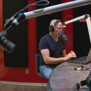 Jason Gregor assis devant un microphone dans un studio de radio.