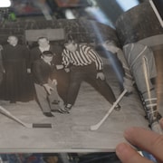 Sur une photo d'époque, jeune homme effectue une mise au jeu protocolaire entre Jean Béliveau et un joueur des As de Québec. 