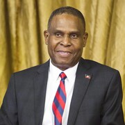 Un homme en complet veston et cravate porte une épinglette aux couleurs d'Haïti