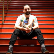 L'auteur, les mains jointes, assis dans l'escalier rouge du théâtre duceppe