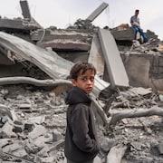Un jeune garçon debout dans les décombres d'un édifice de béton détruit par un bombardement.
