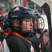 Des filles de profil sur un banc de joueuses de hockey regardent le match. 