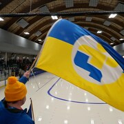 Une personne agite un drapeau géant aux couleurs de l'équipe de l'Est-du-Québec dans un aréna.