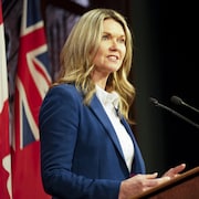 Jill Dunlop durant un point de presse devant des drapeaux du Canada et de l'Ontario.