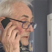 Un vieil homme tient un téléphone à son oreille.