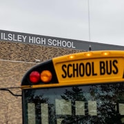 Un autobus scolaire devant une école dont le nom apparaît en grosses lettres blanches sur la façade.