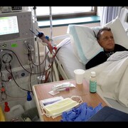 L'homme est couché sur un lit d'hôpital avec une machine de dialyse à ses côtés.