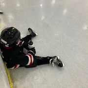 Un jeune joueur est assis sur la glace.