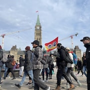 Des personnes manifestent devant le parlement à Ottawa, le matin du vendredi 21 avril 2023, au troisième jour de la grève des fonctionnaires fédéraux. Une personne tient un drapeau de l'Alliance de la Fonction publique du Canada.