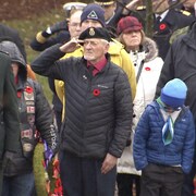 Un homme âgé coiffé d'un béret fait un salut militaire, à côté d'un militaire plus jeune en uniforme faisant la même chose.
