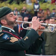 Un militaire joue de la trompette devant une foule.