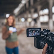 Une femme munie d'un gilet pare-balle parle devant la caméra, un micro à la main.