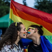 Un couple lesbien s'embrasse sous un drapeau de la communauté LGBTQ+.