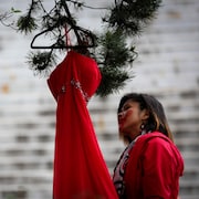 Une personne habillée de rouge a une main rouge peinte sur le visage. Elle est debout près d'une robe rouge accrochée à un arbre.