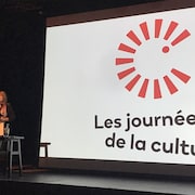 Une femme parle au lutrin devant un écran où est projeté le logo des journées de la culture.
