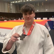 Jean-David Bouchard est devant le tatami et tient une médaille d'or. 