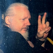 Julian Assange fait le signe de la victoire par la fenêtre d'une voiture.