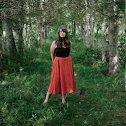 La femme se tient au milieu d'une rangée d'arbres.