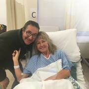 Une femme est dans un lit d'hôpital et son conjoint se tient à côté d'elle.