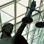 Une statue tient haut dans sa main une balance, symbole de la justice.
