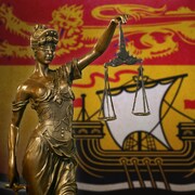 Une statue représentant la justice devant un drapeau du Nouveau-Brunswick.