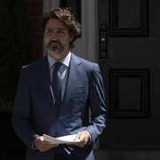Justin Trudeau, devant sa résidence, avec des feuilles en main.