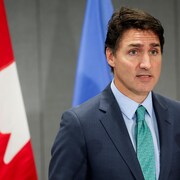 Justin Trudeau parle devant un micro. Derrière lui, il y a deux drapeaux. 