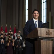 Le premier ministre Justin Trudeau debout devant un pupitre avec en arrière plan les membres de son nouveau gouvernement