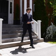 Justin Trudeau sort de sa maison en tenant des feuilles de papier.