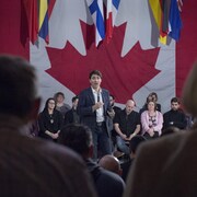 Justin Trudeau parmi une foule devant le drapeau du Canada
