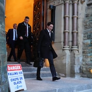 Justin Trudeau sort de l'édifice du parlement, suivi de deux hommes, tandis qu'on voit à ses pieds une pancarte où il est écrit «Danger, chute de glace».