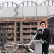Justin Trudeau derrière un lutrin. Derrière lui, un aéroport en ruine.