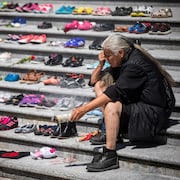 Une femme autochtone se recueille près de souliers d'enfants déposés sur des marches en ciment.