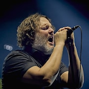 Karl Tremblay, sur scène, chante. Il a une barbe et les cheveux frisés.