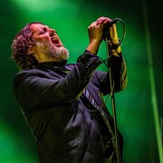 Le chanteur chante dans un micro, entouré d'une fumée verte. 