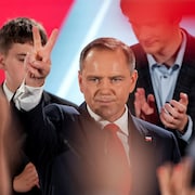 Karol Nawrocki, sur scène devant des partisans, fait un signe de « V » avec ses doigts.